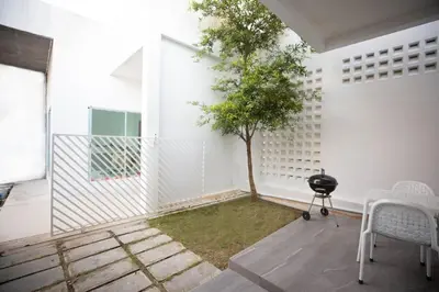 a patio with a tree and a grill and a white wall at Ali Cozy Houses in Ban Thalat Choeng Thale
