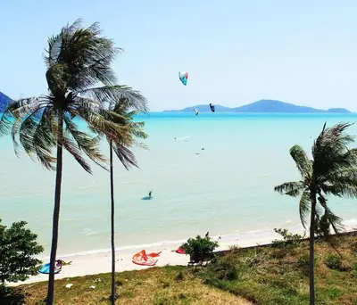 a beach with palm trees and people in the water at Sunrise Beachfront Rawai in Ban Saiyuan (1)