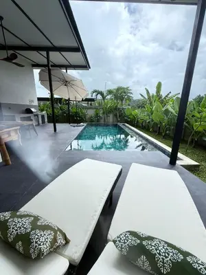 a pool with two white benches and an umbrella at Sakhu Art Villa in Nai Yang Beach