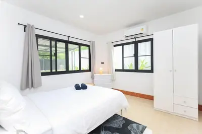 a white bedroom with a white bed and windows at Japanese barnhouse Bang Tao beach in Ban Thalat Choeng Thale