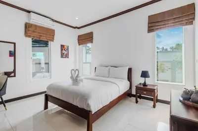 a bedroom with a bed and a table and windows at V267 Newly Renovated 2BR with Pool Near Beaches in Ban Saiyuan (1)