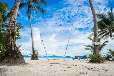 an empty swing on a beach with palm trees at Paradise Koh Yao - Seaview Pool Villa in Ko Yao Noi