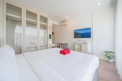 a white bedroom with a white bed with a red bag on it at Studio Apt Seaview Balcony - Oceana C63 in Kamala Beach