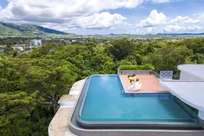 a person sitting on a chair next to a swimming pool at Duplex 1 BR Apt UTL B112 - Direct Pool Access in Rawai Beach