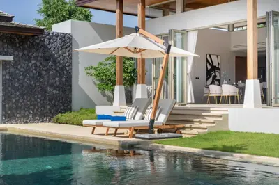 a pool with chairs and an umbrella next to a house at Luxury Royale Bangtao Pool Villa with maid in Thalang