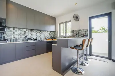 a kitchen with gray cabinets and a counter with chairs at Camellia Pool VillaNear Nai Harn And Rawai Beach in Ban Saiyuan (1)