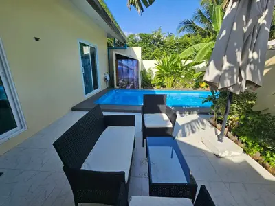 a patio with chairs and an umbrella next to a swimming pool at 2 Bedrooms Tropical Pool Villa Rawai in Rawai Beach