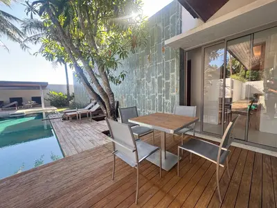 a table and chairs on a deck next to a swimming pool at Anchan Grand Residence Bangtao in Ban Pak Lak