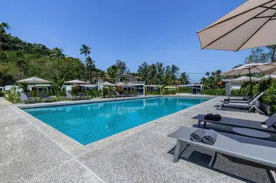 a pool at a resort with chairs and an umbrella at Private Pool Apple House, Sea & Breakfast Bangtao in Ban Lum Fuang