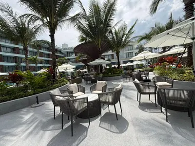 a patio with tables and chairs and palm trees at Sunshine BEACH FRONT access to the pool in Layan Beach