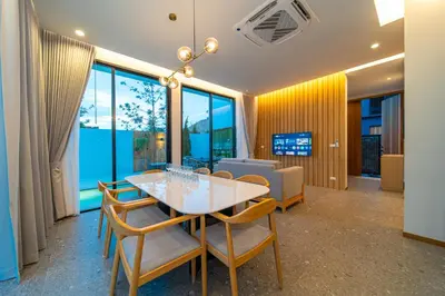 a dining room with a table and chairs and windows at BangTao 4-Bedroom Brand New Modern Luxury Villa 2024 Minimalist Design Spacious 15-meter L-Shaped Swimming Pool Ideal for Guests in Laguna Phuket