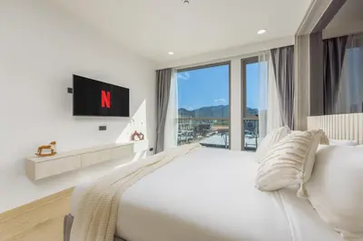 a bedroom with a white bed and a large window at Suite Salina 2BR Pool Gym Access Ozone in Laguna Phuket