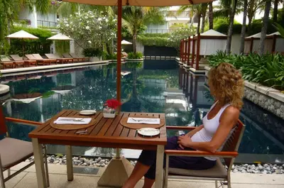 a woman sitting at a table in front of a pool at Beachfront 2 BR Luxury Condominium Surin in Surin Beach