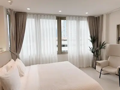 a bedroom with a white bed and a chair and window at Breeze House Patong in Patong Beach