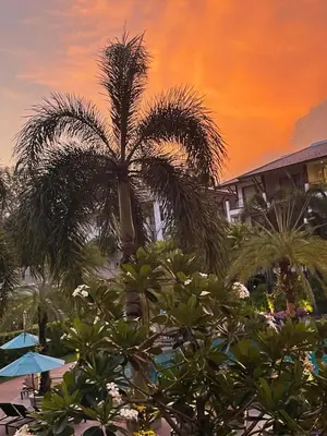 a palm tree in front of a building with a sunset at Beachfront 2BR Apartment with Pool View in Nai Thon Beach