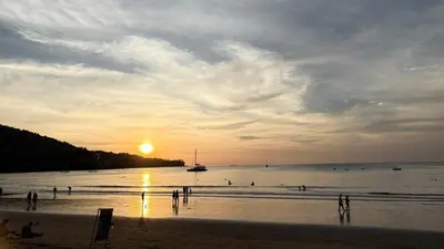 a group of people on the beach at sunset at เดอะ รินรา กมลา ฮัท in Kamala Beach
