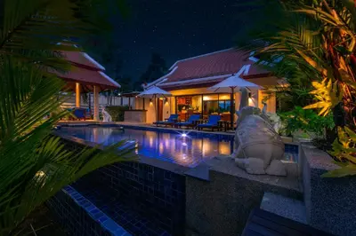 a swimming pool in front of a house at night at Baan Bua Estate Villas by TropicLook in Nai Harn Beach