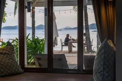 a room with a view of the ocean and a couple sitting at a table at The Cove in Panwa Beach