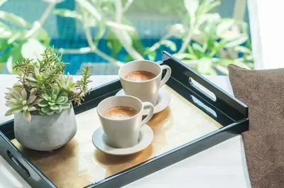 two cups of coffee on a tray with a plant at The Title KR Beach Condotel Rawai Beach in Rawai Beach