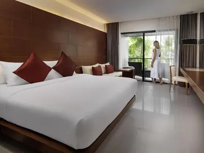 a bedroom with a large white bed and a woman standing in a room at Novotel Phuket Kata Avista Resort and Spa in Kata Beach