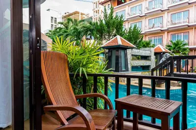 a balcony with a chair and a table and a swimming pool at Nipa Resort, Patong Beach in Patong Beach