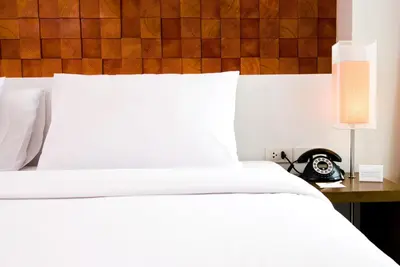 a bed with white sheets and a clock on a table at The Album Hotel in Patong Beach