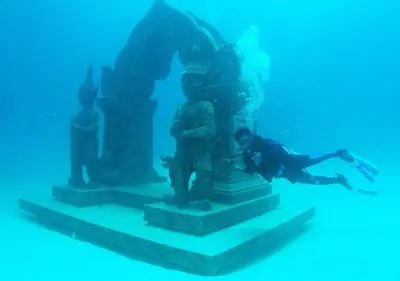 a man is swimming next to a statue in the water at Racha Island Resort (Rayaburi) in Ko Racha Yai