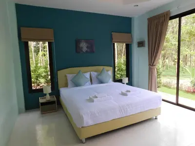a bedroom with a large bed with blue walls and windows at Phuket Sirinapha Resort in Nai Yang Beach