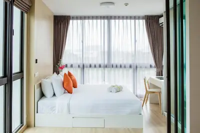 a bedroom with a bed with a desk and a window at Connext Residence Phuket in Phuket Town