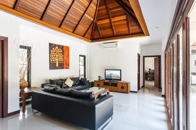 a living room with a black couch and a wooden ceiling at Frangipani pool villa - garden, BBQ & maid in Nai Harn Beach