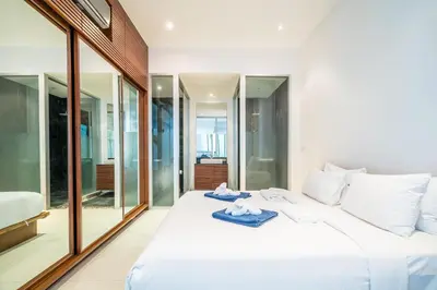 a bedroom with a white bed and glass walls at The Quarter by Lofty in Surin Beach