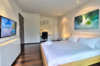 a bedroom with a white bed with a desk and a chair at The Title Comfort Condotel in Rawai Beach