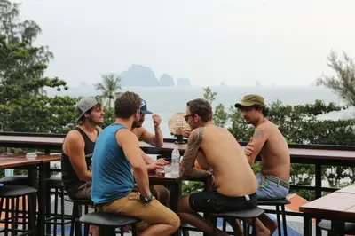 a group of men sitting at a table in front of the ocean at Balcony Party Hostel - 18-40 in Ao Nang Beach