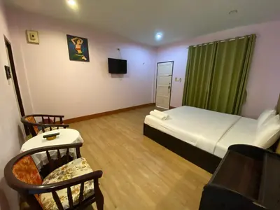 a room with a bed and a tv and chairs at Pachumas Hotel in Karon Beach