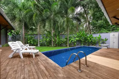 a swimming pool with white chairs next to a wooden deck at VILLA FLORES 3BR Private Pool 10 min to Nai Harn in Rawai Beach