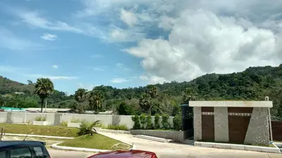 a building in a parking lot with mountains in the background at Naithon condominium A-103 in Nai Thon Beach