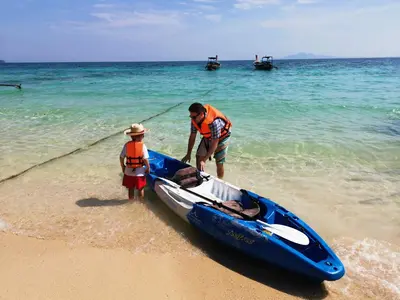 a man and a child standing next to a boat on the beach at Phi Phi Relax Beach Resort in Phi Phi Don
