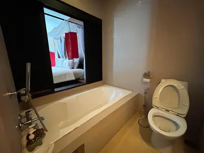 a bathroom with a toilet and a bath tub with a window at Benyada Lodge - Surin Beach in Surin Beach