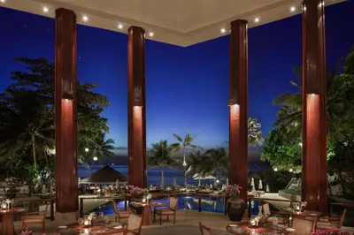 a restaurant with a view of the ocean at night at The Surin Phuket in Surin Beach
