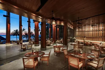 a restaurant with tables and chairs and large windows at The Surin Phuket in Surin Beach