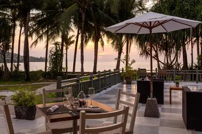 a table and chairs with an umbrella and the ocean at Sunprime Kamala Beach in Kamala Beach