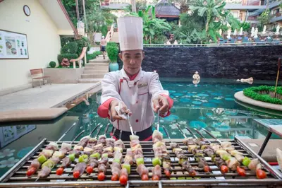 a chef preparing food on a grill in front of a pool at Karona Resort & Spa - SHA Extra Plus in Karon Beach