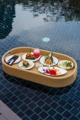 a tray with plates of food on a table by a pool at Villa Zolitude Resort & Spa - SHA Extra Plus in Chalong