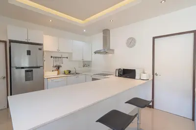 a white kitchen with a counter and two chairs at JUNGLE APARTMENT2 BEDROOMS PRIVATE POOl in Kamala Beach