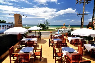 a restaurant with tables and white umbrellas and the beach at Karon Princess Hotel SHA EXTRA Plus in Karon Beach