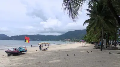a beach with two boats and a flag on it at Sea Beach Paradise in Patong Beach