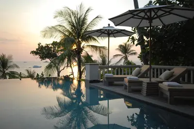 a pool with chairs and umbrellas next to the ocean at Trisara Villas & Residences Phuket in Nai Thon Beach