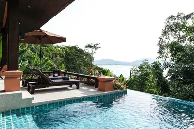 a swimming pool with a chair and an umbrella at Korsiri Pool Villas in Panwa Beach