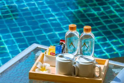 a tray with two bottles and cups and mugs next to a pool at Airport Beach Hotel Phuket in Nai Yang Beach