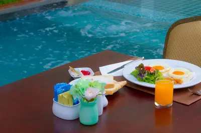 a table with a plate of food next to a pool at Airport Beach Hotel Phuket in Nai Yang Beach
